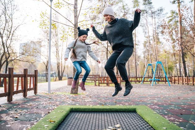 Eine Mutter springt mit ihrer Tochter auf einem Trampolin auf einem Spielplatz im Herbst.
