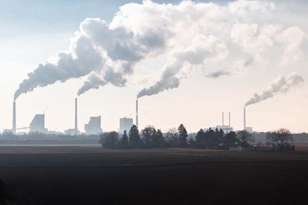 Am Horizont sind mehrere Fabriken zu sehen, aus deren Schornsteinen CO2 austritt.