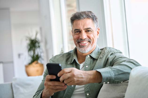 Ein älterer Herr hat sein Smartphone in der Hand und lächelt.
